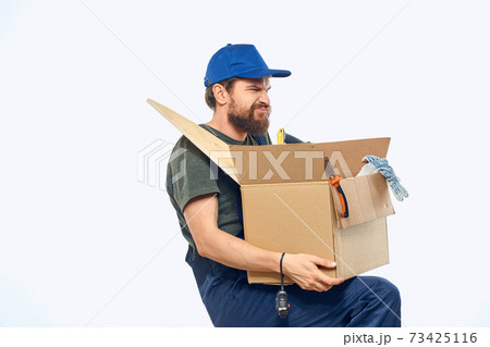 Worker man in uniform with a box in his hands tools delivery service light background Worker man in uniform with a box in his hands tools delivery service light background 73425116