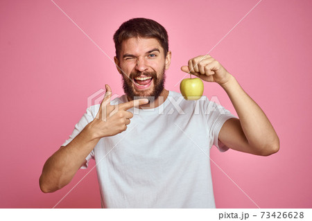 Cute man with an apple on a pink background gestures with his hands cropped white T-shirt Copy Space Cute man with an apple on a pink background gestures with his hands cropped white T-shirt Copy Space 73426628