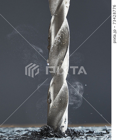 Metal drill bit make holes in aluminum billet on industrial drilling machine with shavings. Smoke rises from the drill. The force of friction. 73428776