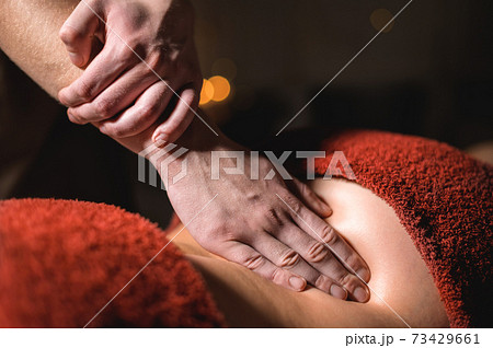 Close-up of a man doing a lower back massage to a woman client in a dark room of a spa massage parlor 73429661