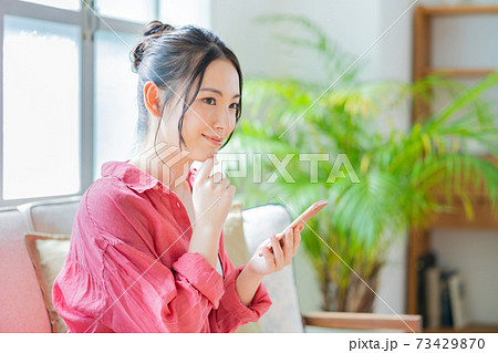ソファでくつろぎながらスマホを操作する女性。 73429870