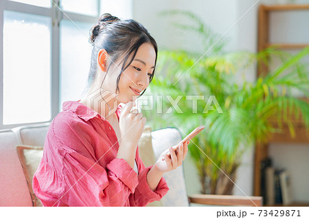 ソファでくつろぎながらスマホを操作する女性。 73429871