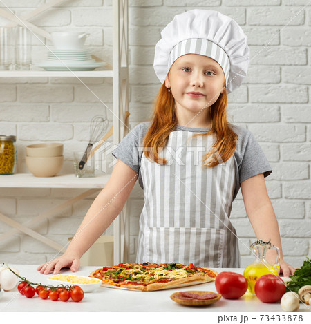 little girl in chef hat and an apron cooking pizza 73433878