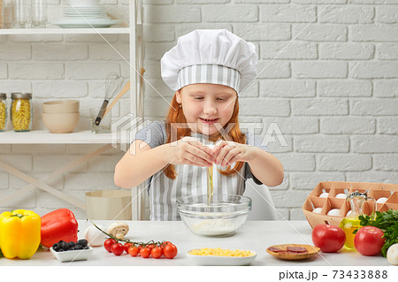 little girl is breaking yellow egg into fresh dough 73433888