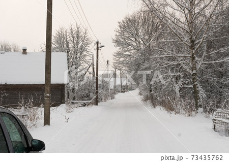Long village road covered with snow, snow on trees, houses in the village, power pole in winter Long village road covered with snow, snow on trees, houses in the village, power pole in winter 73435762