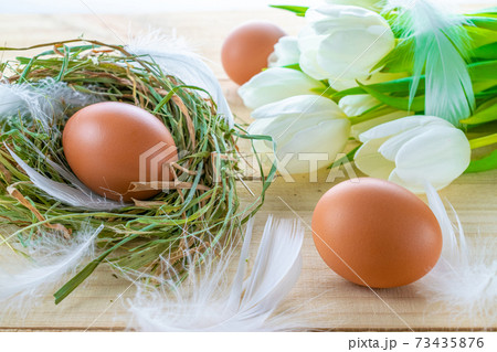 Easter symbol. Natural colour eggs in basket with spring tulips, white feathers on wooden table background in Happy Easter decoration. Congratulatory easter design. Easter symbol. Natural colour eggs in basket with spring tulips, white feathers on wooden table background in Happy Easter decoration. Congratulatory easter design. 73435876
