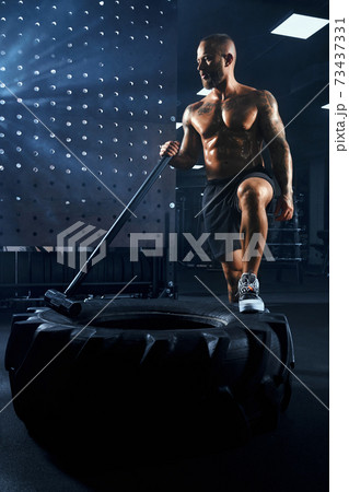Shirtless bodybuilder carrying sledgehammer on wheel. Shirtless bodybuilder carrying sledgehammer on wheel. 73437331