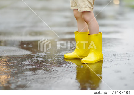 Little boy wearing yellow rubber boots walking on rainy summer day in small town. Little boy wearing yellow rubber boots walking on rainy summer day in small town. 73437401