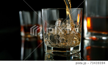 Glass of whisky with splashing liquid and ice rocks inside. Glass of whisky with splashing liquid and ice rocks inside. 73439394