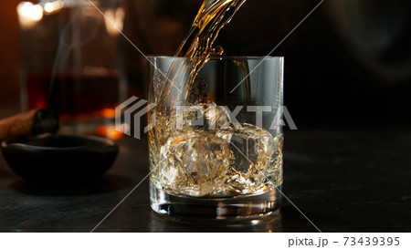Glass of whisky with splashing liquid and ice rocks inside. Glass of whisky with splashing liquid and ice rocks inside. 73439395