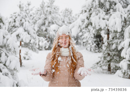 Happy young redhead woman plays with snow in pine tree forest 73439836