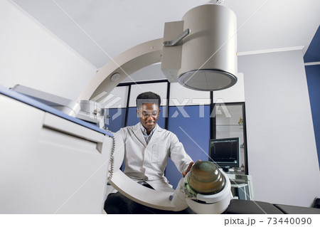 Bottom view of young confident African doctor in white uniform, working with modern lithotripter equipment for treatment of kidney stones. Non-invasive extracorporeal shock wave lithotripsy Bottom view of young confident African doctor in white uniform, working with modern lithotripter equipment for treatment of kidney stones. Non-invasive extracorporeal shock wave lithotripsy 73440090