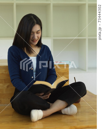 Female student reading book while sitting on staircase in reading corner 73444302