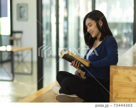 Female student reading book while sitting on staircase in reading corner at university 73444303