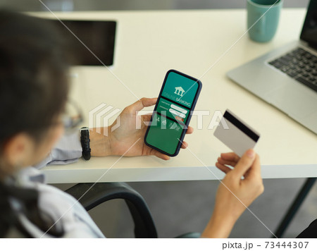 Businesswoman hand holding credit card while online paying on smartphone Businesswoman hand holding credit card while online paying on smartphone 73444307