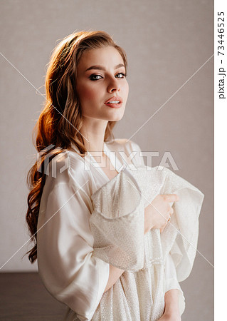 portrait of beautiful woman in white robe holding wedding dress in front of her 73446525
