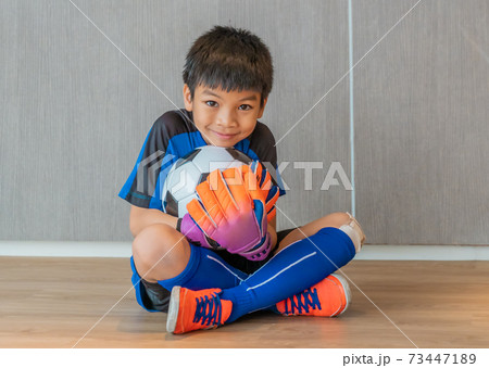 Asian boy is a football goalkeeper wearing gloves and holding a soccer ball with smile face. Asian boy is a football goalkeeper wearing gloves and holding a soccer ball with smile face. 73447189