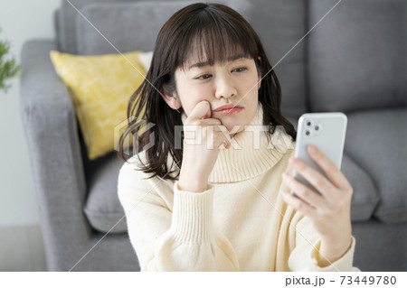 スマートフォンを持って考え込む若い女性 73449780