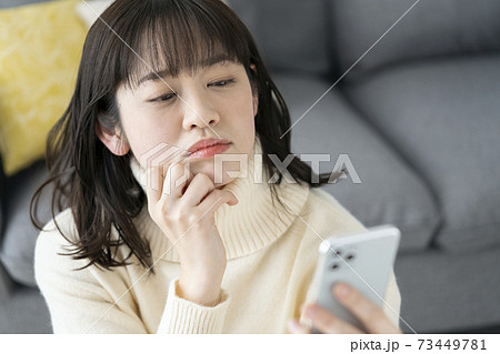 スマホを見て考え込む若い女性 73449781