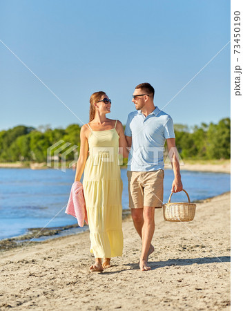 happy couple with picnic basket walking on beach 73450190