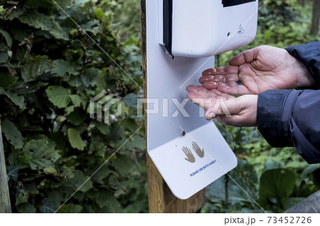 Close up of person using automatic hand sanitizer dispenser during Corona virus crisis. 73452726