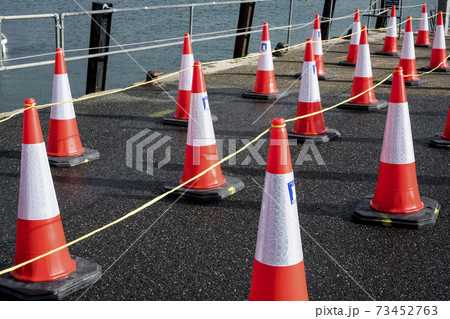Close up of large number of traffic cones lined up on a harbour wall. 73452763