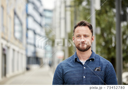 Man with a beard standing outdoors in a city on a quiet street 73452780
