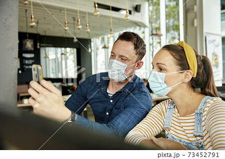 Two people wearing face masks, using a smart phone, waving during a face time call. 73452791