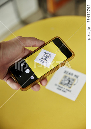 A person uisng a smart phone, taking a photograph of a Track and Trace QR code on a yellow background 73452792