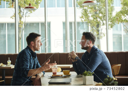 Two men seated in a cafe talking, having a meeting. 73452802