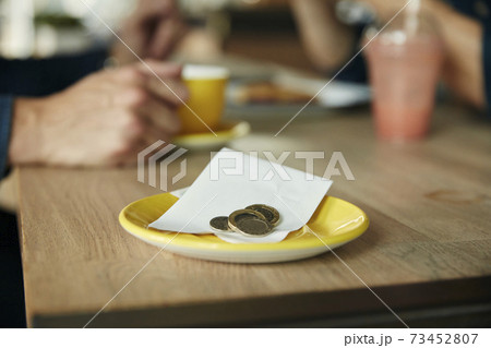 A small saucer with a till receipt and coins, cash on a cafe table. 73452807