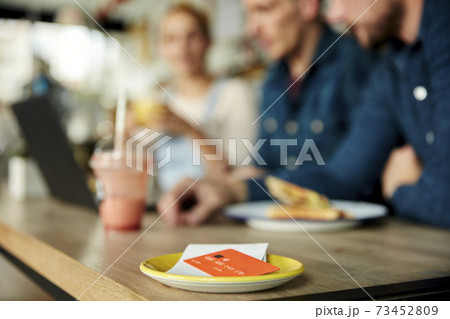People at a cafe table, a saucer with till receipt and credit card. 73452809