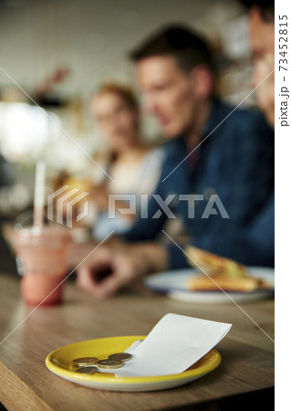 People at a cafe table, a saucer with till receipt and cash payment 73452815