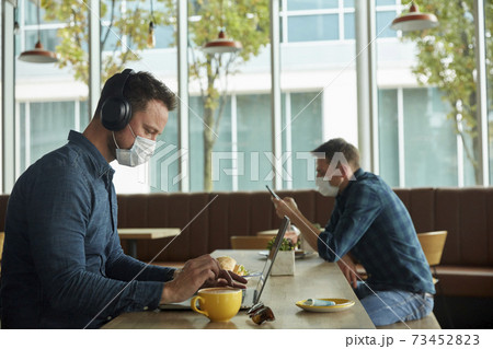 Two men seated in a cafe, working remotely using a laptop and smart phone 73452823