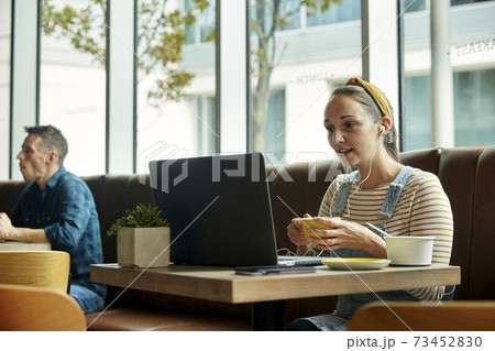 Woman seated in a cafe using a laptop interacting during an online call 73452830