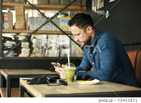 Man sitting alone at table with laptop and juice drink in cafe using smart phone 73452871