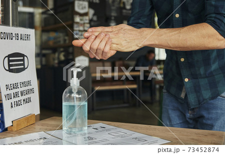 Man rubbing hands together using hand sanitiser in restaurant 73452874