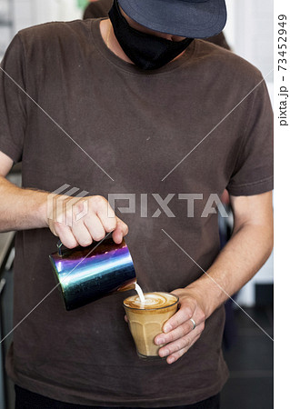 Close up of male barista wearing face mask pouring cafe latte. 73452949