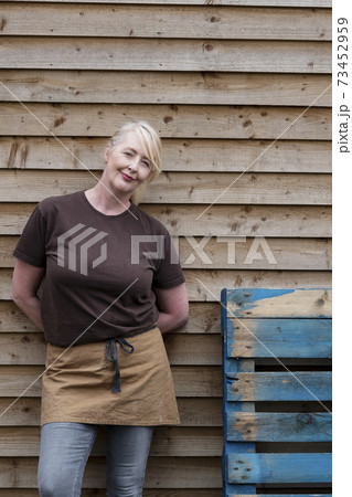 Portrait of waitress wearing brown apron, leaning against wall, smiling. 73452959
