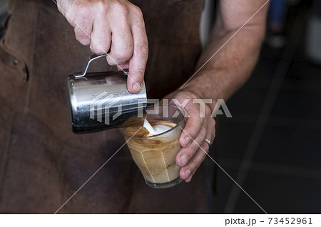 Close up of barista wearing brown apron pouring cafe latte. 73452961