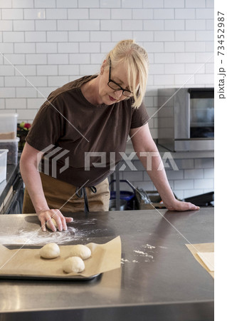Woman in brown apron standing in a cafe kitchen, mixing baking danish pastry dough 73452987