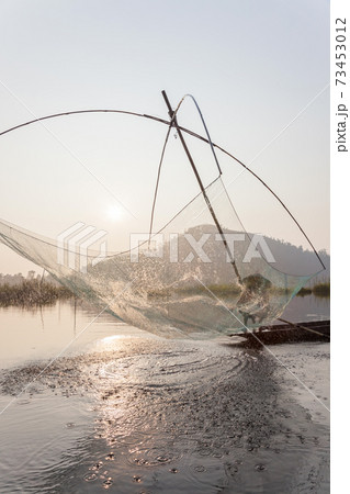 Fisherman on his boat moving arched swing nets above the water at Loktak Lake 73453012