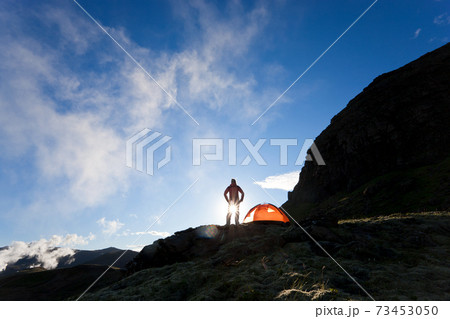 Woman standing by tent at sunrise, Iceland 73453050
