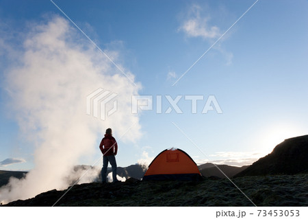 Woman standing by tent at sunrise, Iceland 73453053
