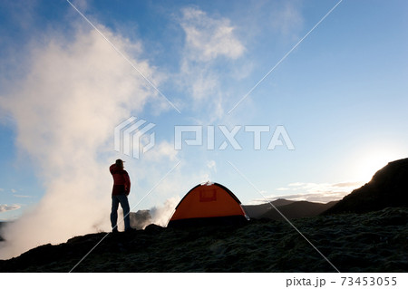 Woman standing by tent at sunrise, Iceland 73453055