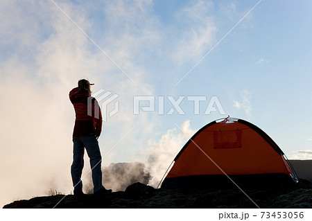Woman standing by tent at sunrise, Iceland 73453056