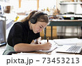 Teenage girl wearing headphones using a laptop and writing in a notebook 73453213