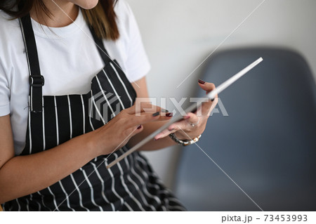Cropped shot of cafe owner sitting in her coffee shop and using digital tablet. Cropped shot of cafe owner sitting in her coffee shop and using digital tablet. 73453993