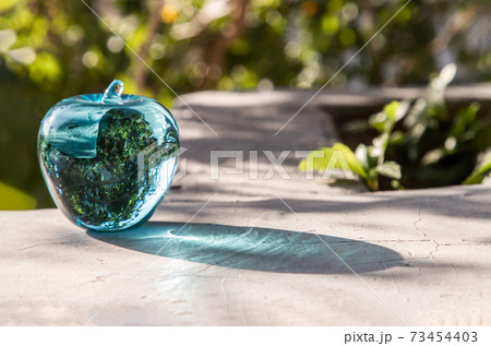 Glass/Crystal blue apple and reflective surface on a natural green background. Glass/Crystal blue apple and reflective surface on a natural green background. 73454403