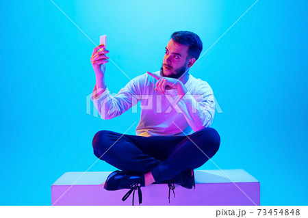 Caucasian man's portrait isolated on blue studio background in neon light. Concept of human emotions, facial expression, sales, ad. Caucasian man's portrait isolated on blue studio background in neon light. Concept of human emotions, facial expression, sales, ad. 73454848